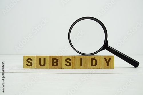 Photos SUBSIDY alphabet letters with magnifying glass on wooden background
