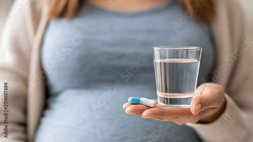 Pregnant woman enjoying a moment of refreshment with a glass of water and vitamins in a cozy setting Generative AI