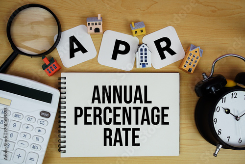APR Annual Percentage Rate text written on notepad with house model, alarm clock and magnifying glass on wooden background