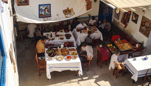 Overhead view of people dining at long tables in a traditional taverna with shared platters