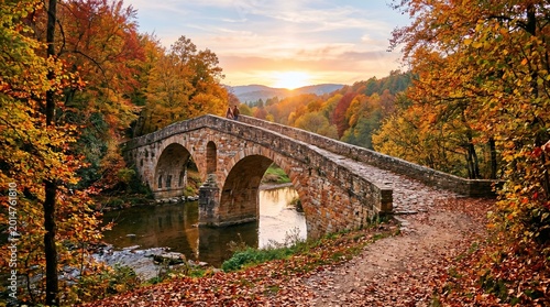 An ancient arched bridge crafted from colorful stones in earthy tones of rust, tan, and gray, spanning a gentle stream. Surrounded by vibrant autumn trees with red, orange, and gold leaves, fallen lea