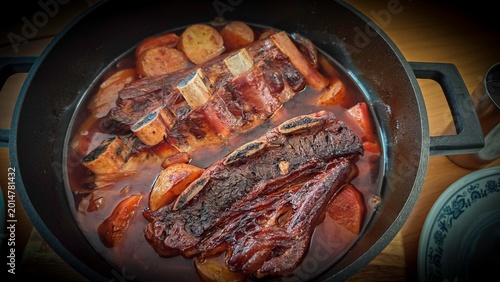 Top View of Slow Cooked Asado Beef Ribs in Rich Broth with Potatoes, Sweet Potato and Onion Boiling in Black Pot, Rustic Gourmet Meat Stew, Comfort Food Close Up