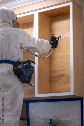 Vertical shot of Worker using a spray gun to apply paint or coating cabinet during renovation.