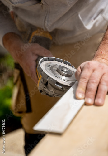 Worker is cutting a ceramic tile with an electric grinder on a workbench during a home renovation project. 