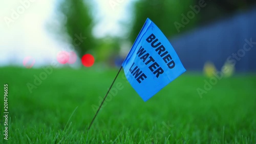 Blue buried water line utility marker flag in grass. safety warning. Close up 