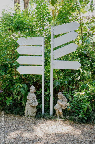 An artistic signpost in a beautiful garden. The signpost indicates directions, standing next to statues