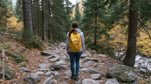 Small explorer carrying a yellow pack while trekking through a vibrant autumnal woodland path on a rocky terrain.
