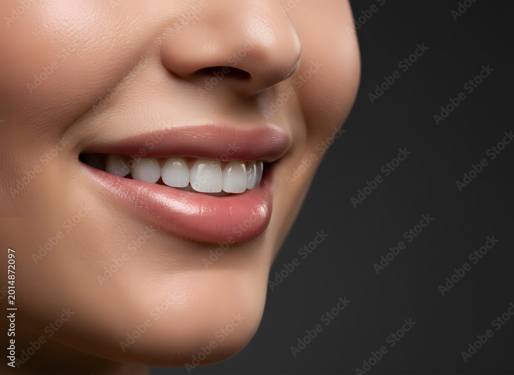 Naklejka premium Close-up profile of a woman with perfect white teeth and glossy lips smiling gently, showcasing healthy oral hygiene and a confident, happy expression against a dark studio background