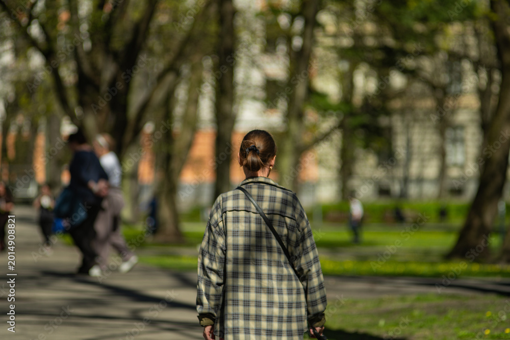 Obraz premium Unrecognizable person walking through sunny urban park with soft focus background and spring atmosphere