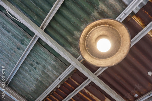Foto A brightly lit light bulb in an old, rusty metal lampshade, mounted on a worn corrugated iron roof, creates a very strong industrial, vintage, or rustic feel