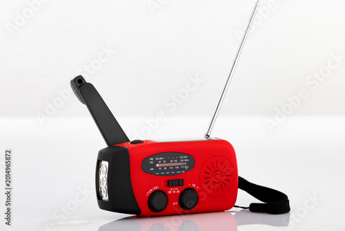 Portable emergency crank radio with flashlight and antenna isolated on light background. Studio product photography for survival, disaster preparedness and emergency concepts.