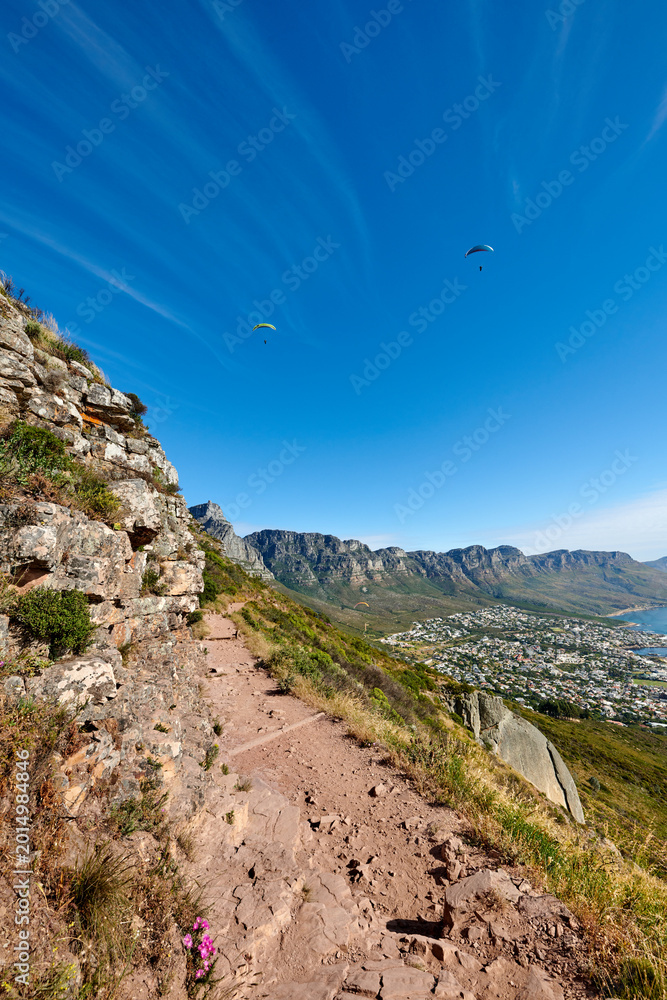 Obraz premium Mountain, hiking trail and travel outdoor, paragliding or blue sky with path to explore. Terrain, hill and trekking environment for adventure, sightseeing and destination with space on cliff