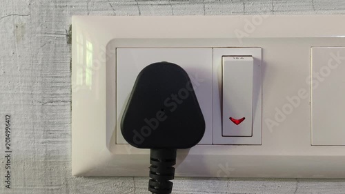 Closeup of hand pushing electric appliance three pin plug into indian power outlet or socket hole on wall and switch on the equipment. Daily household electricity consumption and use concept.