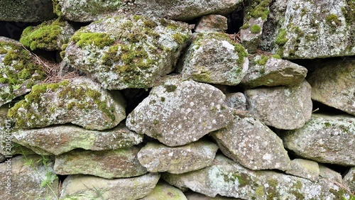 Weathered dry stack stone wall showing natural texture with green moss and white lichen