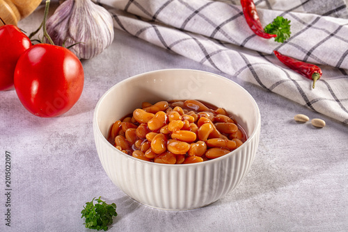 Homemade baked beans in a white bowl with fresh tomatoes, garlic, and chili peppers on a gray background
