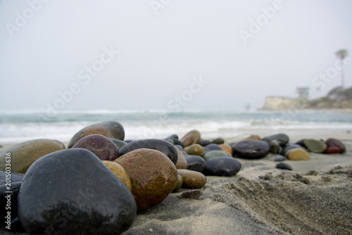 Close up of wet colorful pebbles on a sandy beach with blurred ocean waves and misty sky background