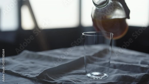 Slow motion pour orange juice into tumbler glass on linen cloth