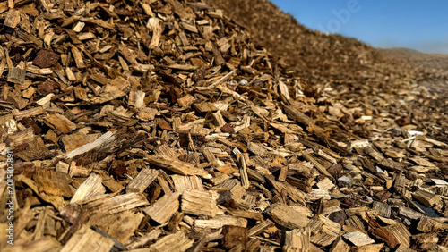 Pile of wood chips in a sunny outdoor setting with clear blue sky and distant hills visible, showcasing natural materials used in landscaping and construction