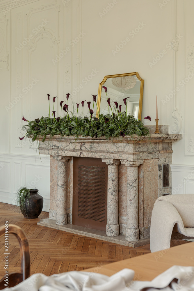 Fototapeta premium Elegant Room Decor: Gold Mirror, Greenery, and Dark Calla Lilies Adorn a Classic Marble Fireplace in a Bright Interior