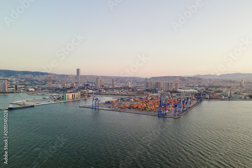 Drone view of cargo port infrastructure with container storage area and bulk terminal. Industrial waterfront and international shipping operations at sunset