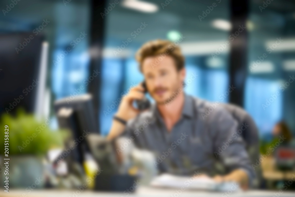 Fototapeta premium Blurred Businessman talking on phone at modern office desk