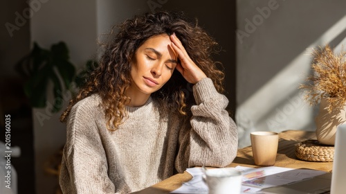 Mindful woman resting at home office desk, feeling stress relief and burnout prevention in warm natural light, with papers, laptop, and coffee cup