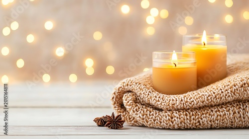 Two burning candles on a folded knitted blanket next to star anise spices