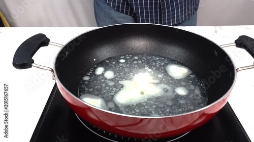 Sprinkling Salt into Red Nonstick Pan with Melted Butter on Electric Stove, Cooking and Recipe Preparation, Close-up of a person sprinkling salt from a small white bowl into a red nonstick pan