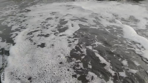 Close-up of foamy ocean waves gently receding from a dark, wet shoreline, capturing the raw power and serene beauty of the sea's rhythmic movement on the beach