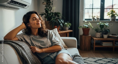 Young Woman Relaxing on Sofa Enjoying Cool Air from Air Conditioner.