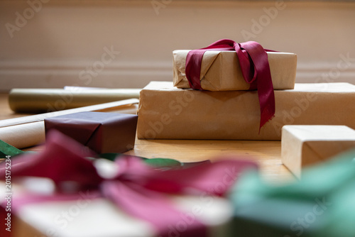Stack of two kraft wrapped gifts sitting on light wood tabletop with burgundy ribbon