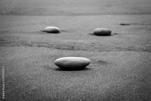 Fotografija Black and white close-up photograph of smooth pebbles resting on dark sand