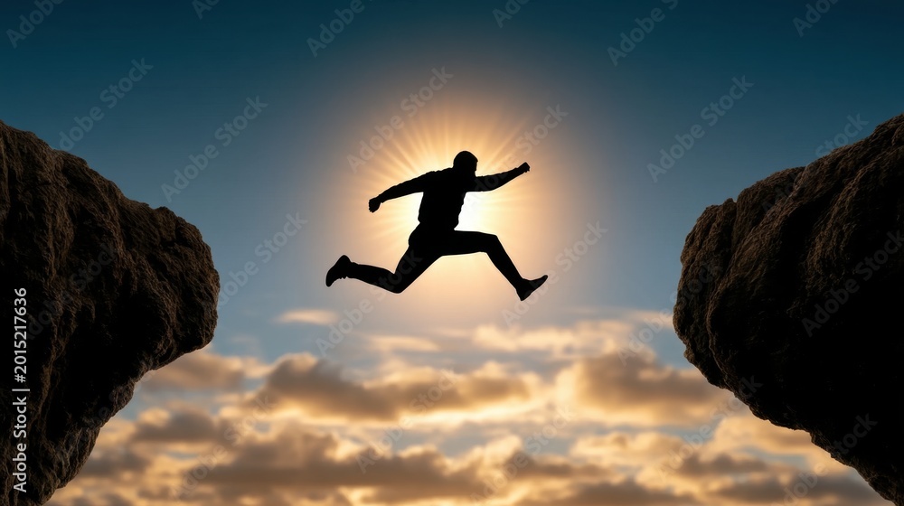Fototapeta premium Silhouette of a person jumping across a gap between two cliffs with the sun shining behind and a cloudy sky in the background at sunset or sunrise