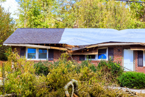 Damaged house with roof covered by tarp after storm in residential area