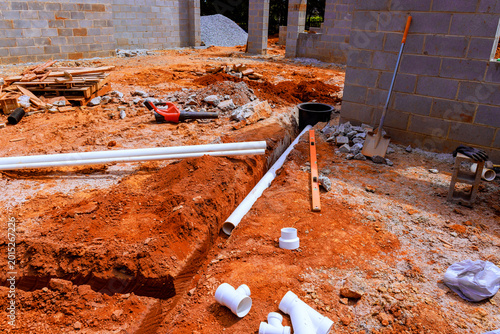 Schilderij op canvas Construction site dug trench with pipes, tools on red soil landscape during wast