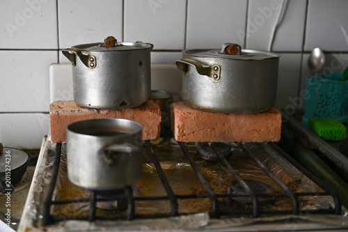 Canvastavla metal pots on stove, elevated with bricks for makeshift heating, kitchen setting in home without central heating, improvising warmth with alternative methods during winter cold