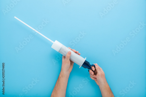 Fotografija Young man hands holding and showing universal plastic syringe for lawnmower engine oil change on light blue table background