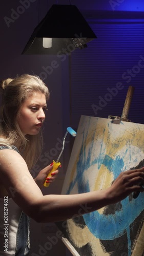 female artist making a painting on a canvas using painter spatula working on a new artwork in her art studio.