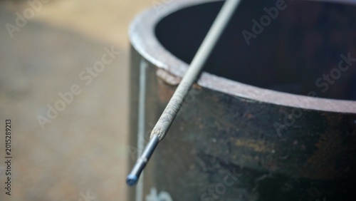 Fotografija Close-up of welding rod resting on metal barrel in workshop setting