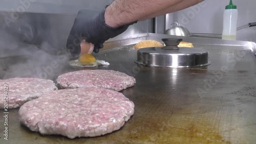 Preparazione di un panino hamburger su piastra. Panino hamburger grigliato con pancetta, cipolla glassata, formaggio e uova