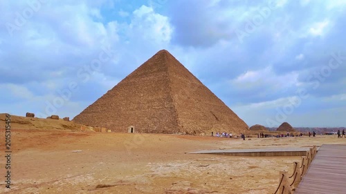 Historical great pyramid of giza under a cloudy sky. Majestic ancient egyptian monument in the desert with people walking on the sand