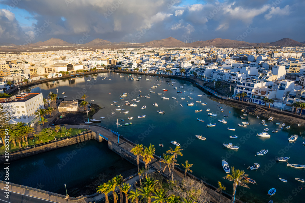 Fototapeta premium Discover the coastal view of Arrecife in Lanzarote. This location features buildings along the waterfront, palm trees, and distant mountains. Enjoy the vibrant atmosphere and unique architecture.