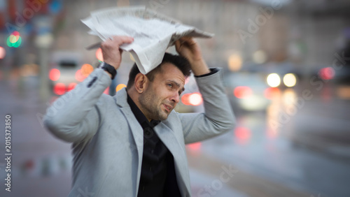 Fotografía Stressed businessman hiding from heavy rain under newspaper with copy space