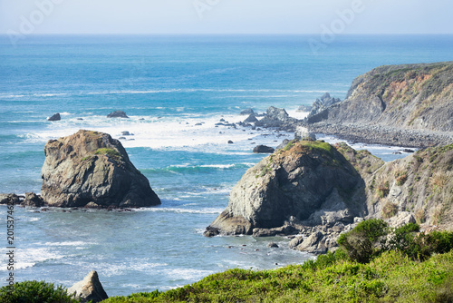 Rocky shoreline along California coast with sea stacks and gentle Pacific waves. Coastal cliffs and natural textures create a calm and scenic ocean landscape