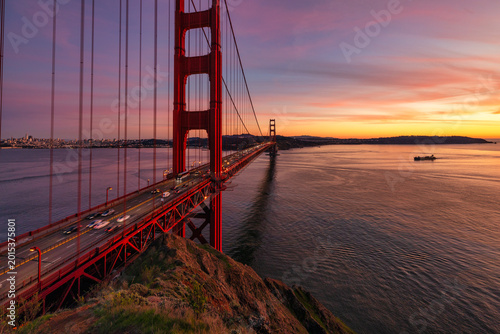 Golden Gate Bridge at sunset in San Francisco with long exposure light trails and vibrant pink sky reflecting over calm bay waters