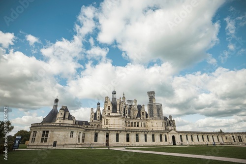 Basking in soft daylight, the grand chateau showcases intricate architectural details amid lush greenery, evoking the charm of a summer escape in the heart of France