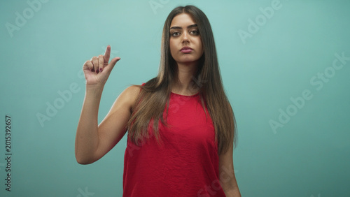 Bilde på lerret Woman pinching fingers to show small size while wearing red tanktop against a teal studio backdrop; indifference measurement