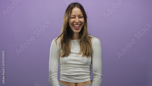 Canvas Print Woman smiling with visible midriff and relaxed posture in studio against purple wall wearing white crop top and jeans; happiness