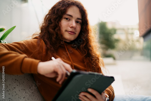 Caucasian redhead man sitting outdoors using digital tablet with stylus looking at camera, creative professional working on project, digital nomadic lifestyle, online education, 5G connection.