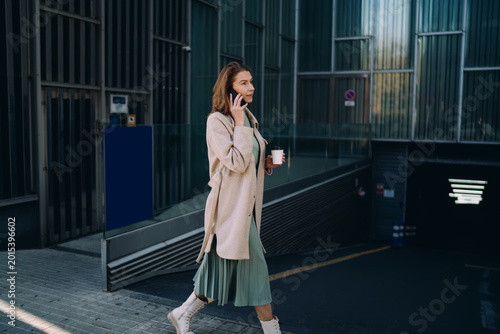 Elegant mature woman talking on smartphone while walking near modern glass building. Successful business professional using cellular network for mobile call outdoors in the city. Career mobility.
